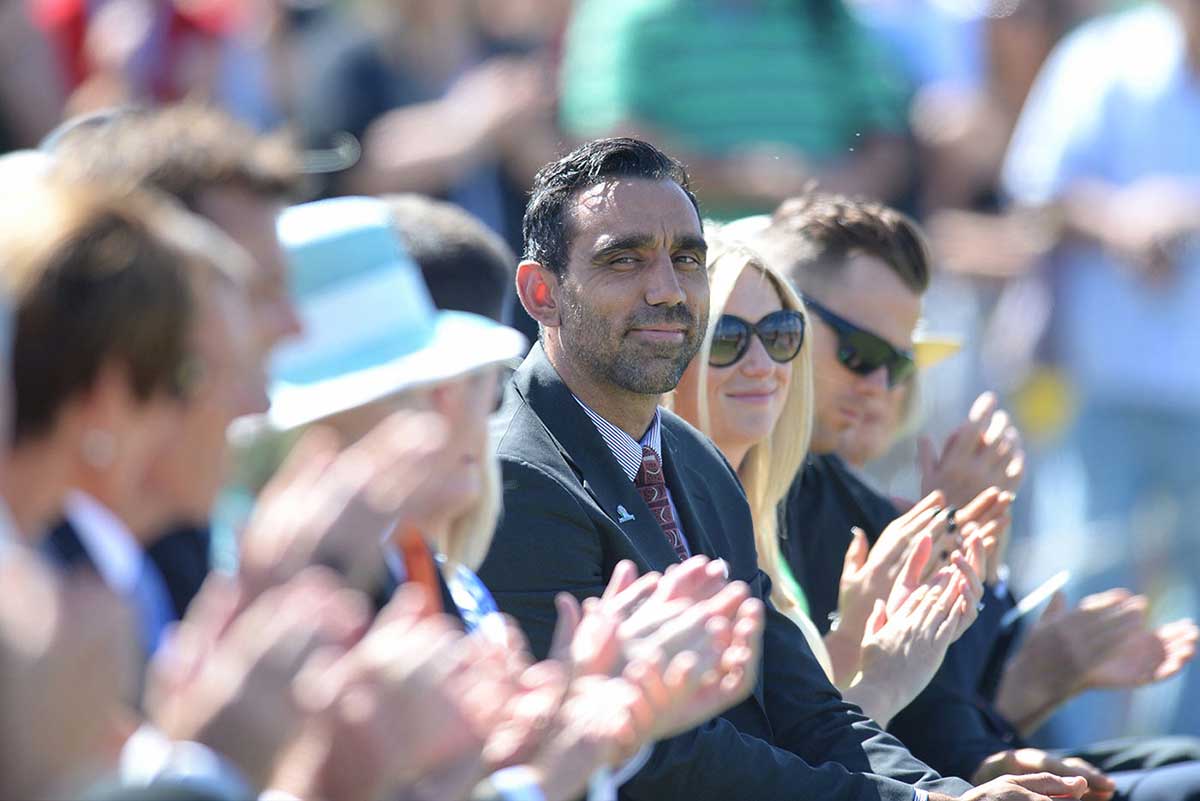 Colour photo of Adam Goodes sitting with an audience in an official ceremony.