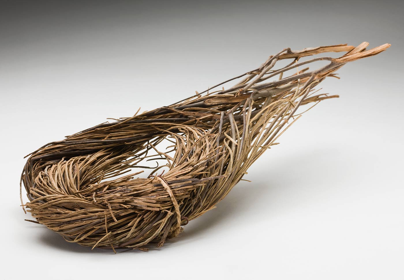 Head pad from the South Australian Museum Collection Description	An undyed grass and twig tear drop like shaped head pad. Two bunches of twigs and grasses have been twisted and folded over to form the tear drop like shape with their ends crossed and protruding. Two tags are attached with string. - click to view larger image