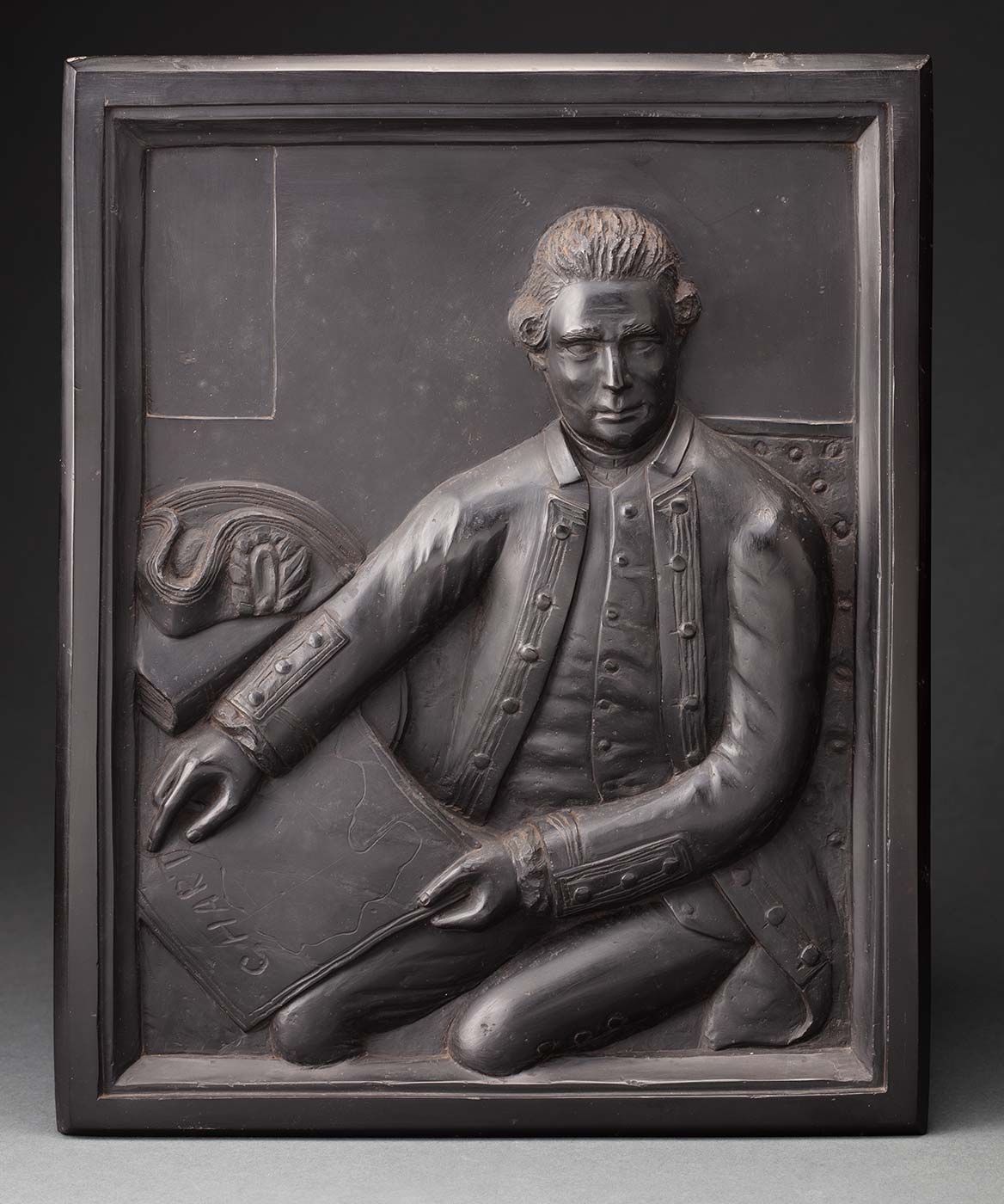 Portrait plaque carved from kerosene shale, depicting Captain Cook in relief, seated ( facing the viewer) and holding a chart. - click to view larger image