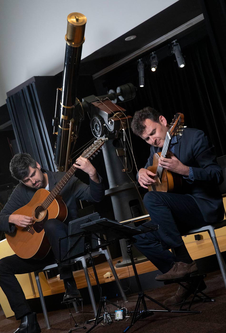 Slava and Leonard Grigoryan play guitars in front of a large telescope. - click to view larger image