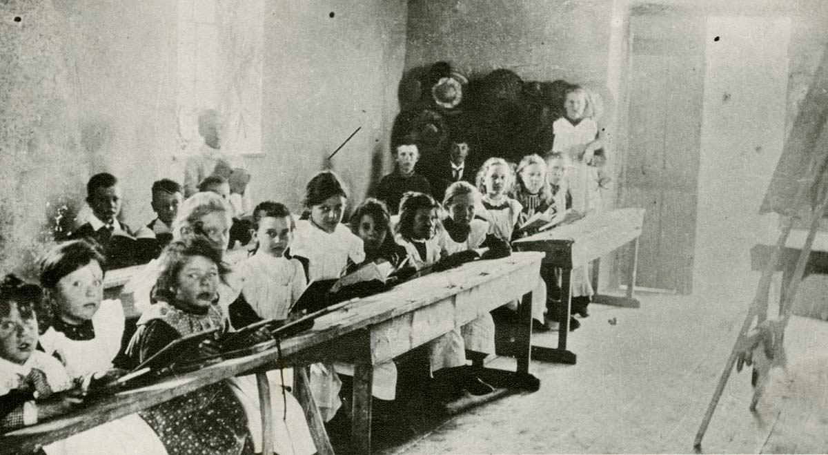 Black and white photograph of school children sitting at desks in a school room.