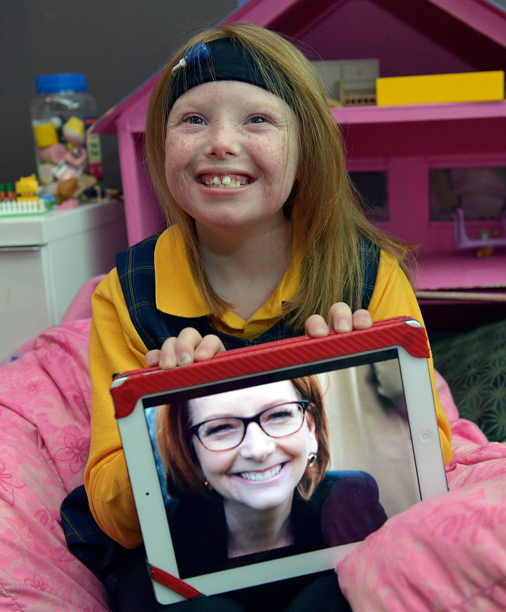 A young girl with a big smile sits on a pink beanbag displaying a photograph of Julia Gillard. - click to view larger image