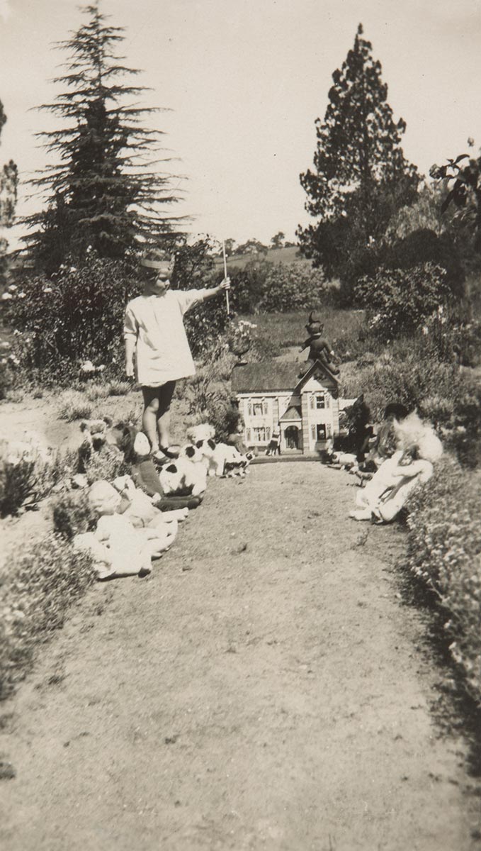 Black and white photograph of a young girl with many toys in a garden. - click to view larger image