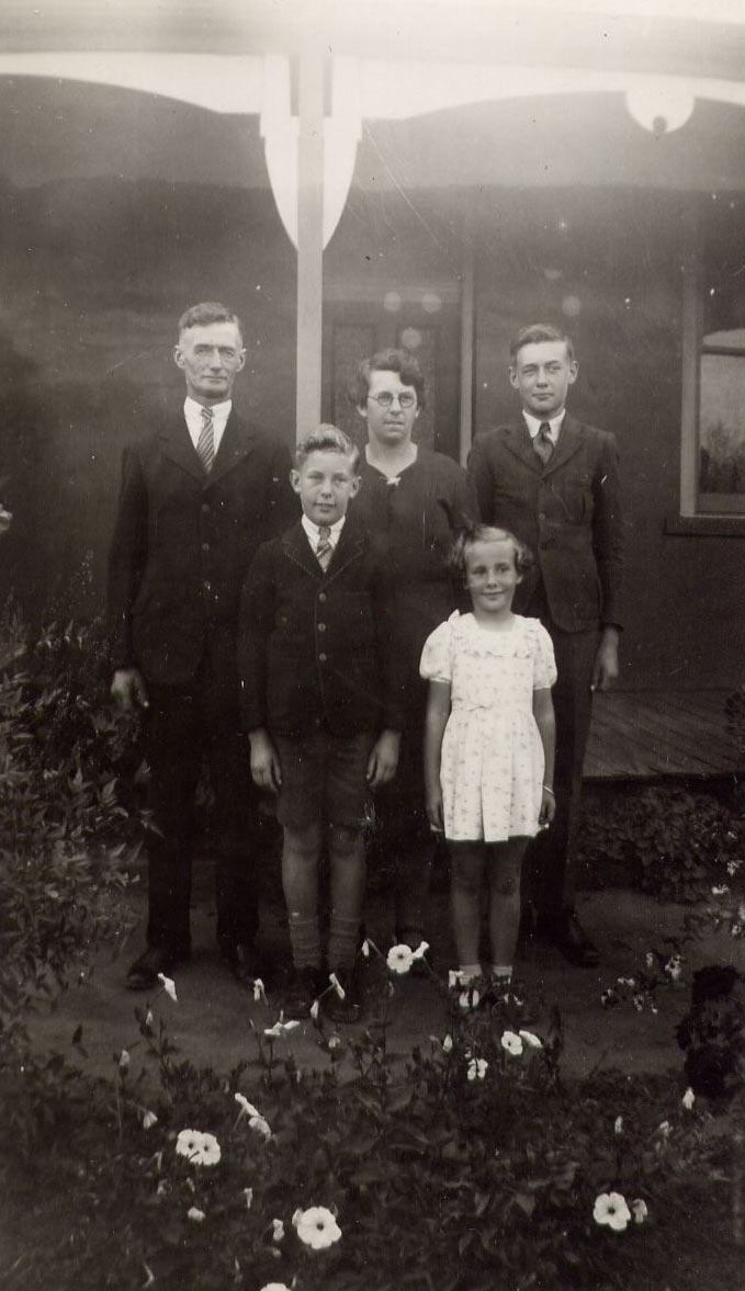 Black and white photograph of a man, woman and three children posing in front of a porch. - click to view larger image