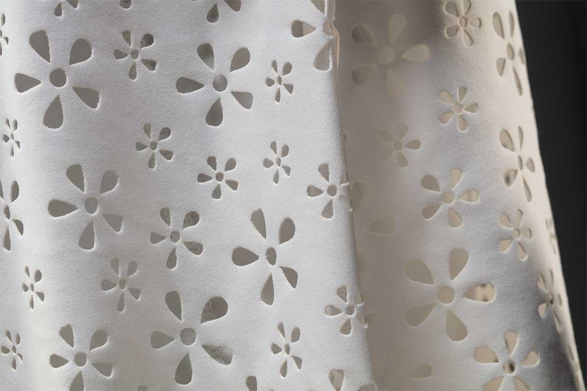 Detail of white fabric with laser cut floral decoration. - click to view larger image