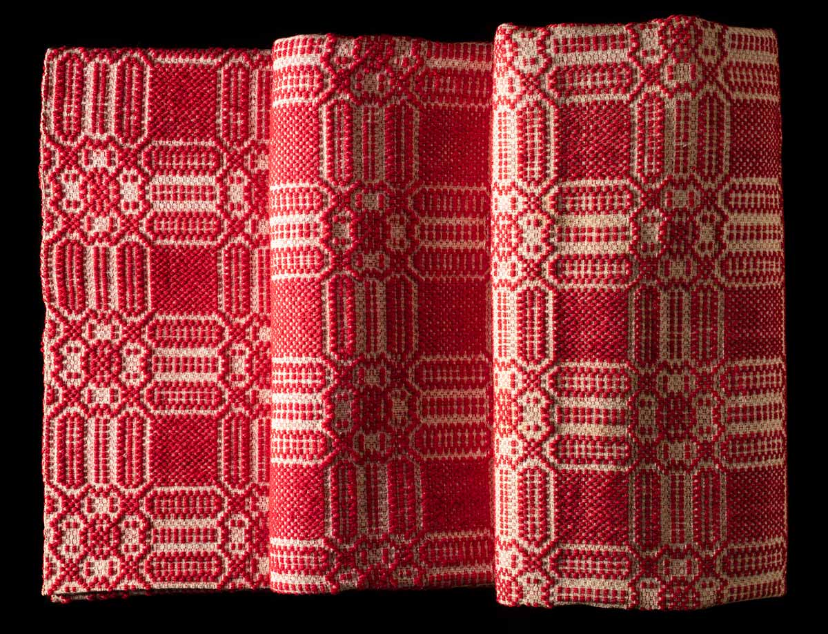 Large red woven bedspread with beige threaded geometric square design.