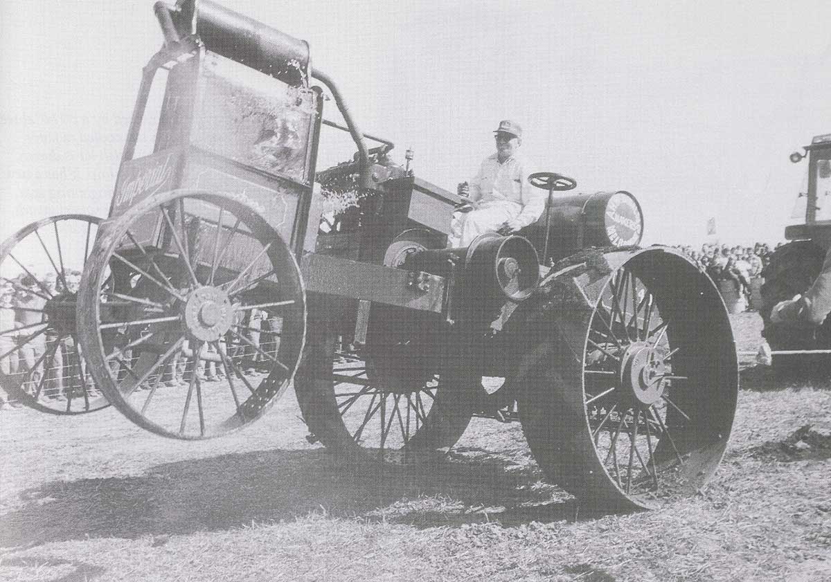 Black and white photograph of a man on a tractor with its front wheels suspended off the ground.   - click to view larger image