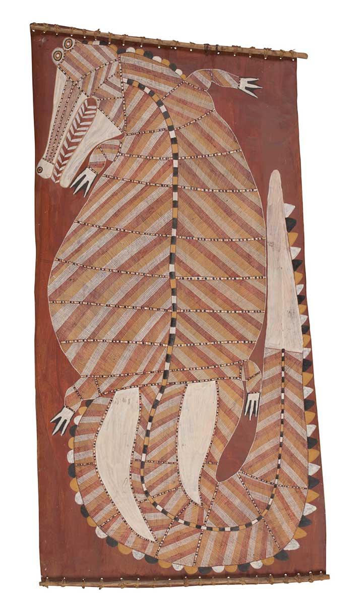 A bark painting worked with ochres on bark and on wooden restrainers. It depicts a crocodile with its head turning to the left and its tail curled up to the right. The crocodile has a yellow, white and brown crosshatched design with white feet, tail, and lower jaw. The painting has a red background. - click to view larger image