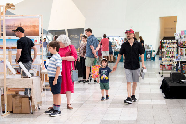 A man holds the hand of a child, while walking through an airy space with market stalls and other people on either side. - click to view larger image