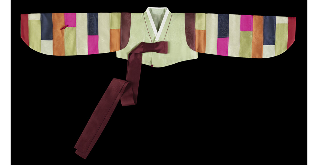 Saekdong jeogori, crafted from green-hued silk with a saekdong, a sleeve adorned with multiple-colored patchwork, designed by Lee Young-hee, 1980s   A fully extended jacket, with thick, vertical stripes in an array of colours.