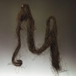 Black human hair loosely and unevenly twisted into a long bundle, partly in loops.