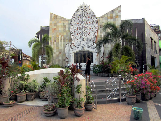 A memorial wall with pot plants in foreground. The names of the victims are listed on a black plaque. - click to view larger image