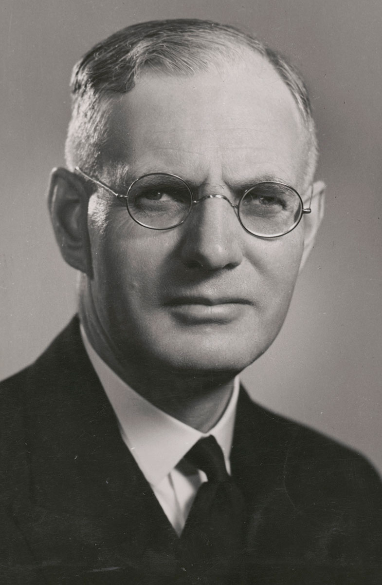 studio black and white photo of Curtin. He is wearing a dark suit and glasses