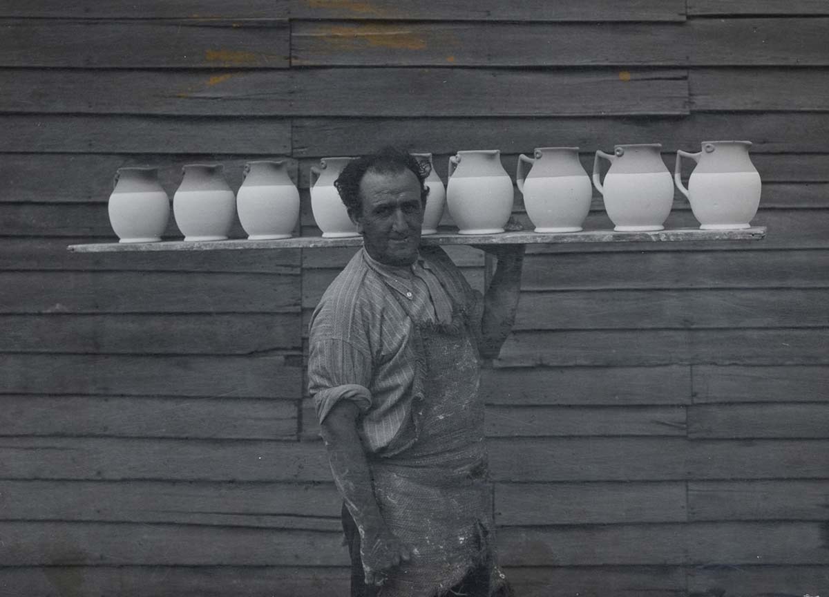 Photograph of Pottery employee H Dower carrying a board laden with jugs.