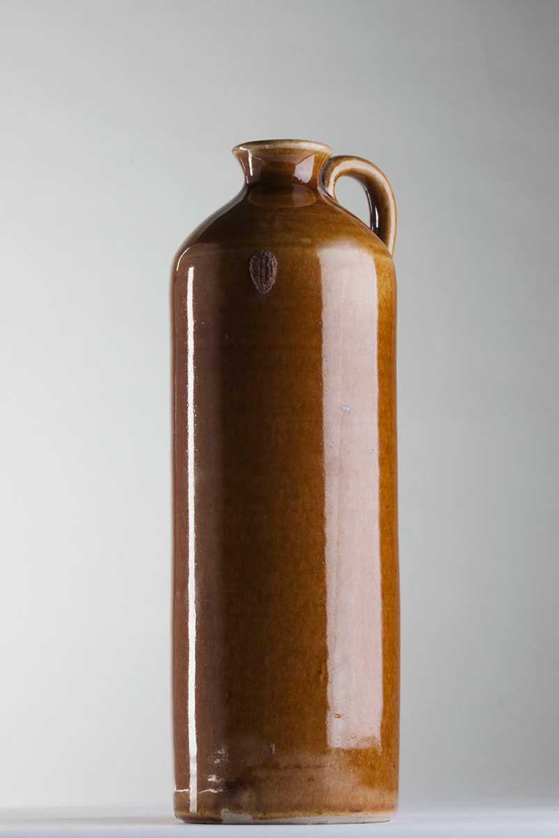 Two cylindrical honey brown glazed vessel. A jug with straight sides tapering to narrow neck and a single handle attached at neck and shoulder. - click to view larger image