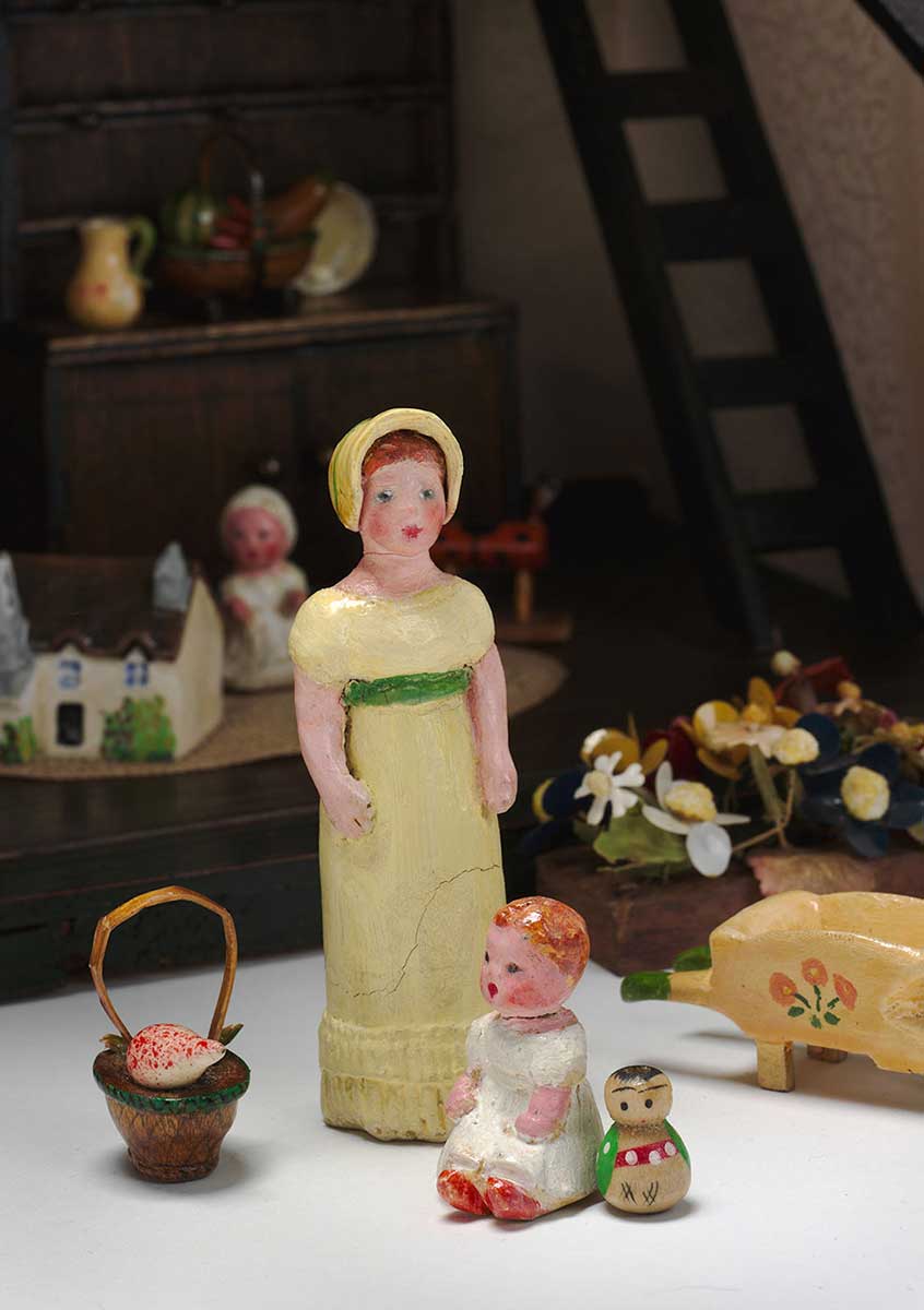 Miniature figures of a young woman and a baby, a basket and flower cart. - click to view larger image