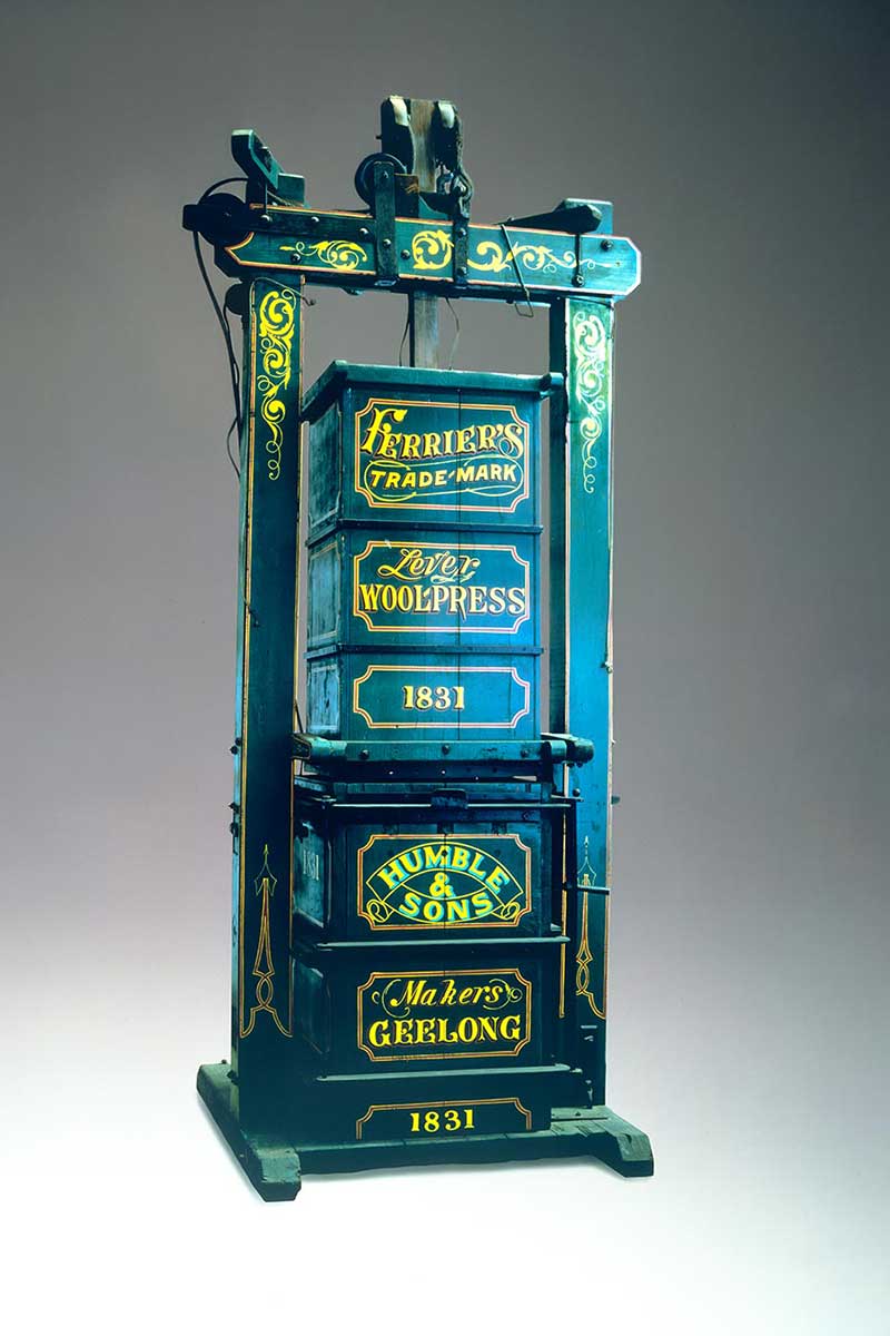 Double box wool press with a central pole and a conical drum rope winch or fuzee. It is painted green with 'FERRIER'S / TRADE-MARK / Lever / WOOLPRESS / 1831 / HUMBLE / & / SONS / Makers / GEELONG / 1831' in yellow on the front. - click to view larger image