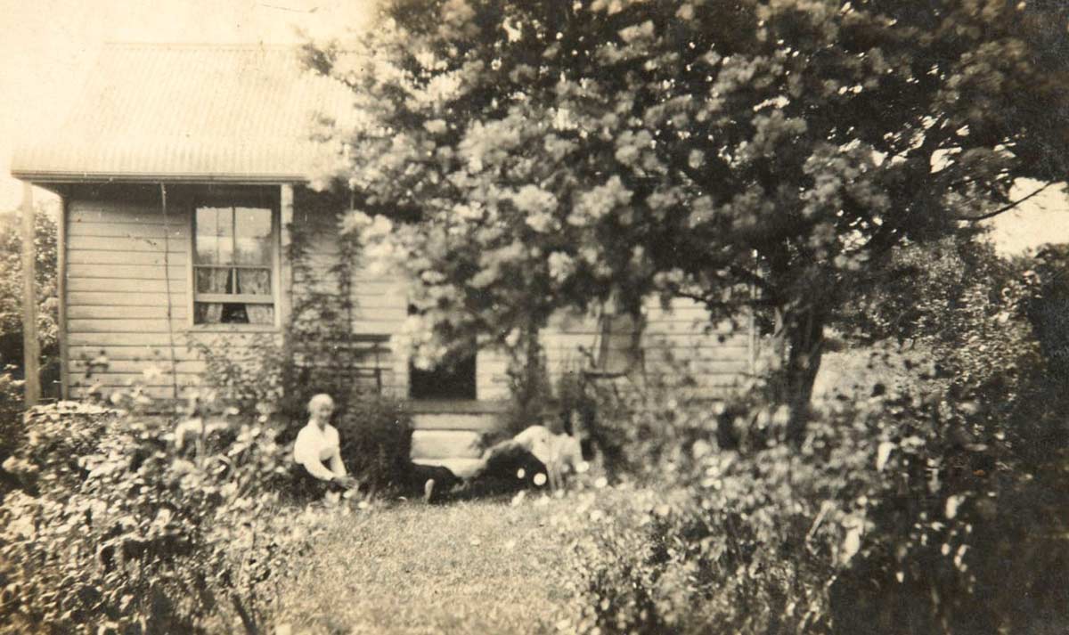 Black and white photograph of a woman and man outside a small weatherboard house.