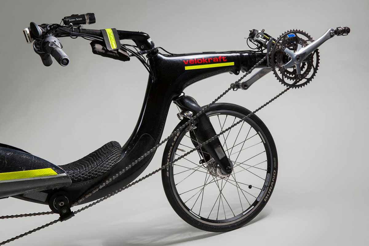 Colour photo showing the side view of the front section of a recumbent bike, with handlebars, front wheel, crankset and part of the chain. - click to view larger image