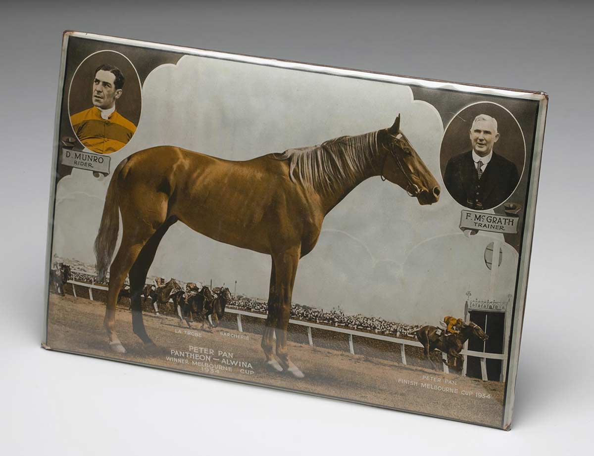 Tin plaque showing side view of a racehorse with the text underneath: 'PETER PAN, PANTHEON-ALWINA, WNNER MELBOURNE CUP, 1930'. Portraits of two men are inset, top left 'D MUNRO, RIDER' and top right 'F McGRATH, TRAINER'.