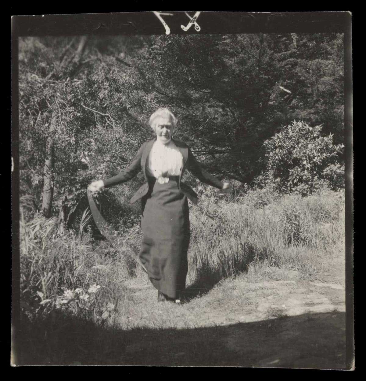 Black and white photograph showing an elderly woman jumping with a rope in a garden. - click to view larger image