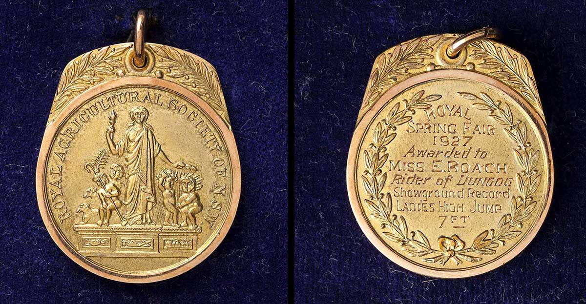 A gold coloured metal medal from the Royal Agricultural Society of N.S.W Royal Spring Fair of 1927. The main section of the medal is circular in shape with an oblong addition at the top that has a small circular hole in the centre. A metal ring is attached through the hole. The medal features a relief picture of a figure, possibly a muse of agriculture standing atop a pedestal amongst four smaller figures bearing symbols of agriculture such as a sheaf of wheat and livestock. Embossed around the circumference of the medal is block text that reads 'ROYAL AGRICULTURAL SOCIETY OF NEW SOUTH WALES'. On the other side of the medal within a relief of a laurel wreath are the engraved markings 'ROYAL / SPRING FAIR / 1927 / Awarded to / MISS E. ROACH / Rider of DUNGOG / Showground Record / LADIES HIGH JUMP / 7 FT'. Laurel branches feature on both sides of the oblong section at the top of the medal. The medal is attached by its ring to the medal box. - click to view larger image