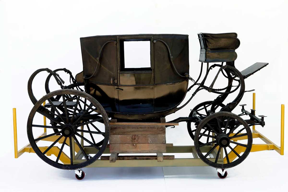 Wooden horse-drawn coach, painted black, with four wheels and mudguards, and Coachman seat at front. 