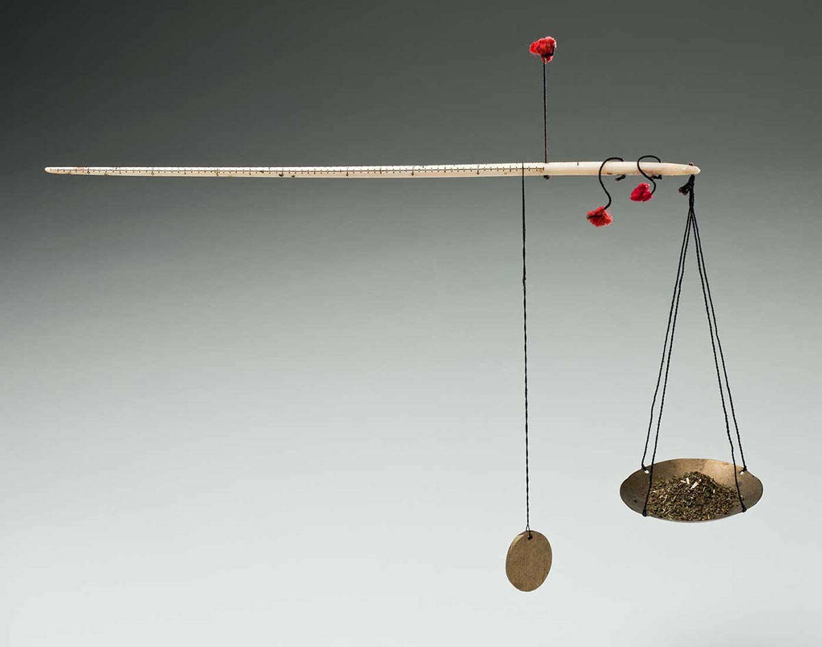 Colour photograph of a set of small scales with a long white rod at top and a small disc hanging at one end, alongside a suspended concave tray. Small pieces of a gold-coloured substance are piled on the tray. - click to view larger image