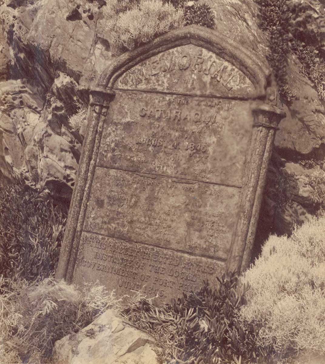old photo of what looks like a gravestone amid bushes on a rocky coast - click to view larger image