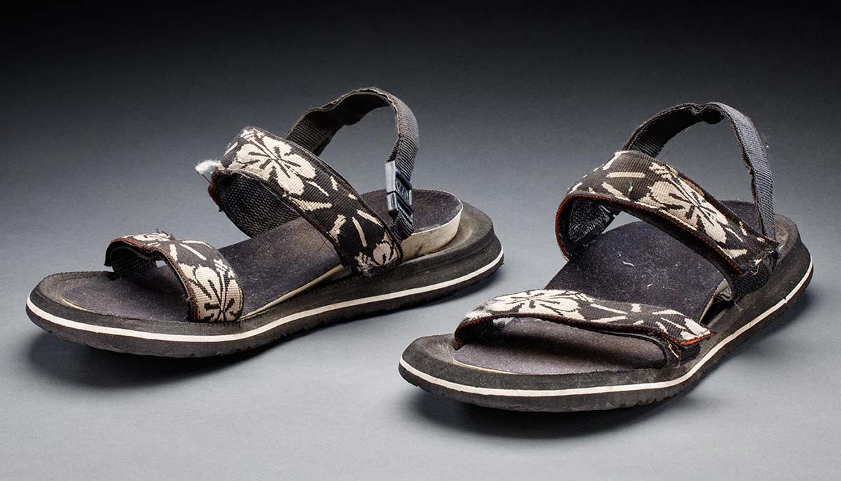 A pair of black, rubber 'reef' style sandals with white hibiscus print on the straps. - click to view larger image