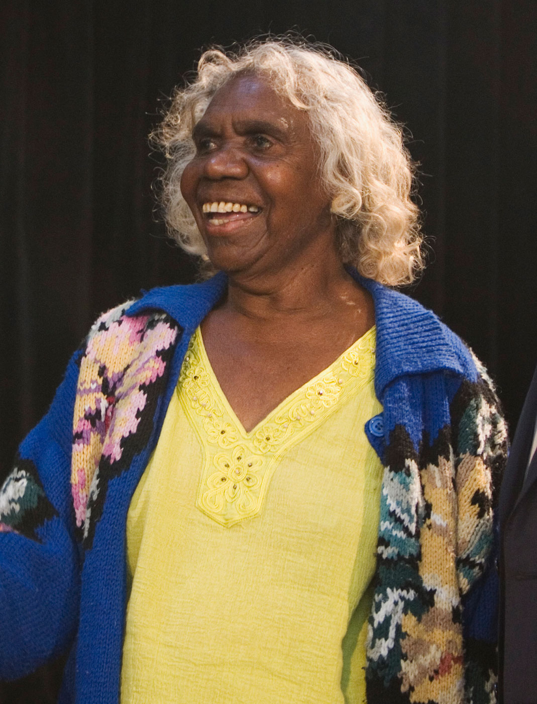 Photo of an Aboriginal Australian woman wearing a yellow T-shirt and smiling. - click to view larger image