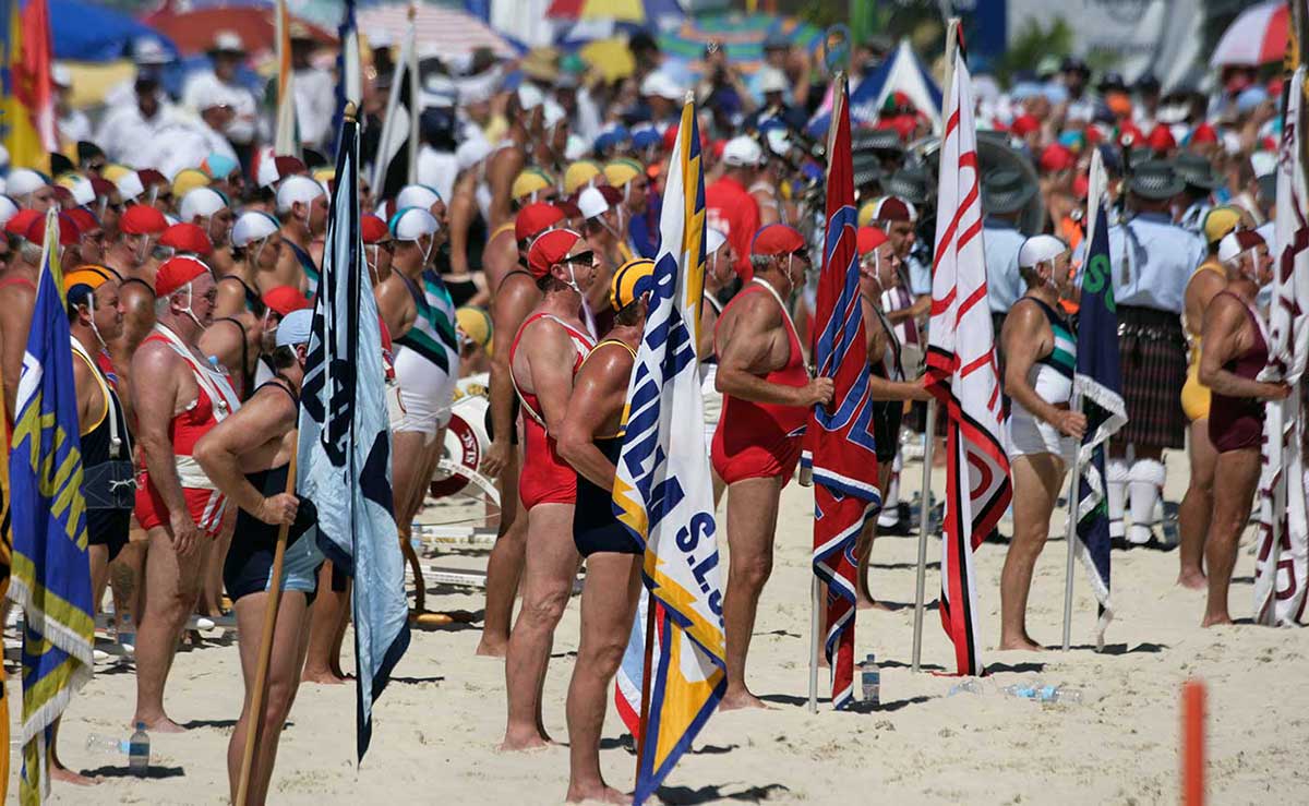 Surf lifesavers standing on the beach in their club costumes and holding their club flags. Australian Surf Life Saving Championships, Kurrawa, Queensland, 2006.