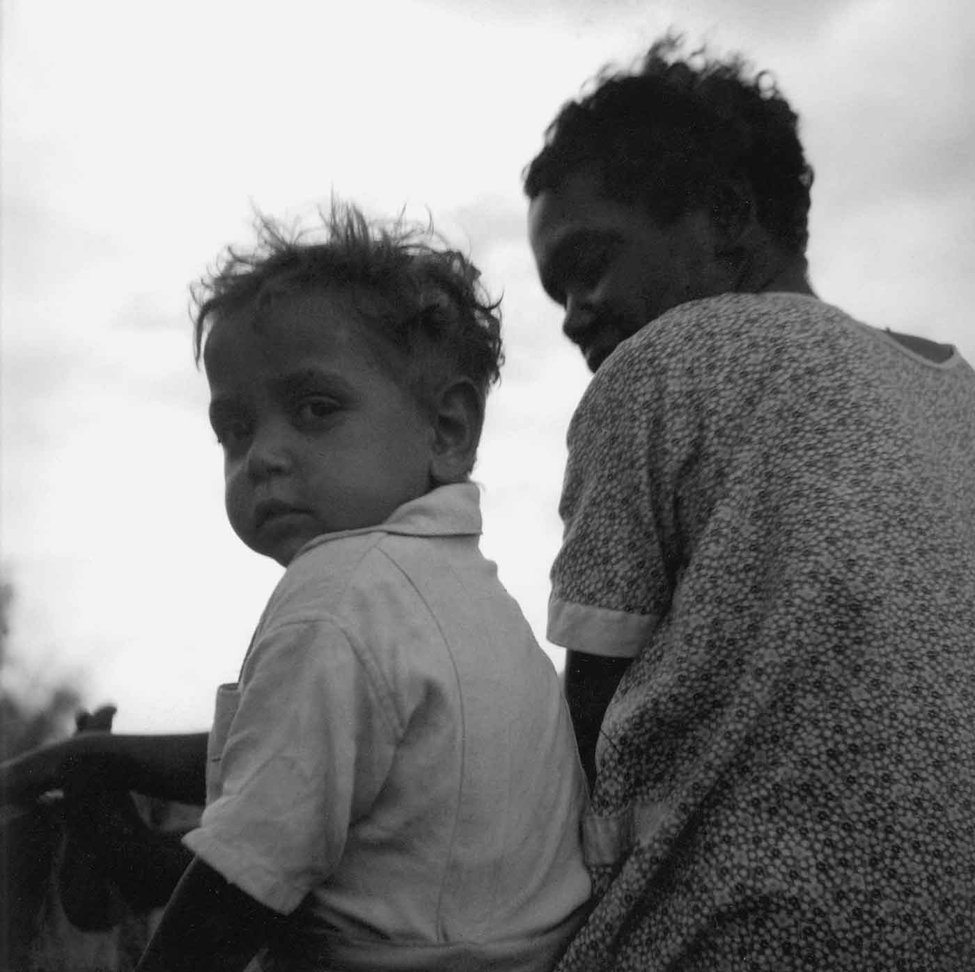Black and white photo of a young First Australian boy seated next to a First Australian woman. - click to view larger image
