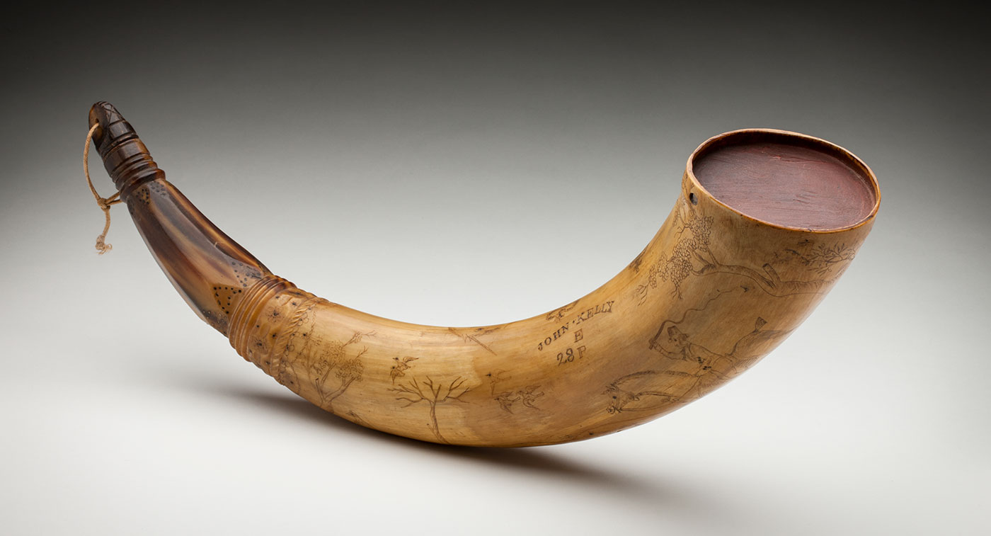 A powder horn, tapering to one end, inscribed with text 'John Kelly, E, 28P', and scenes of a man riding on a horse among trees.