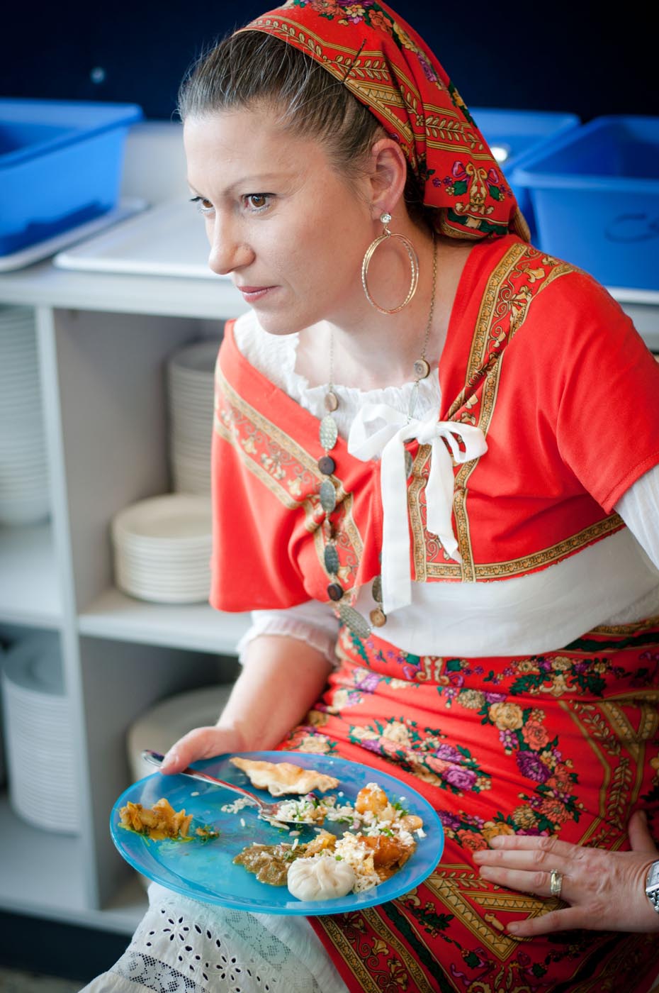 Photo showing a lady wearing her national costume seated with a plate of food on her lap - click to view larger image
