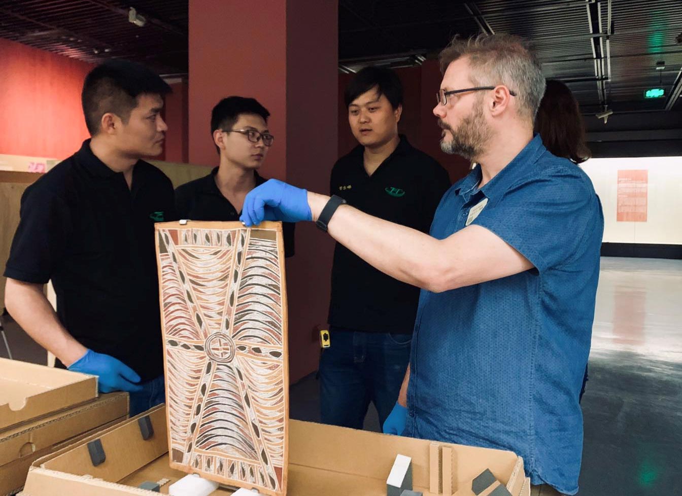Four men inspect a bark painting in a gallery. - click to view larger image