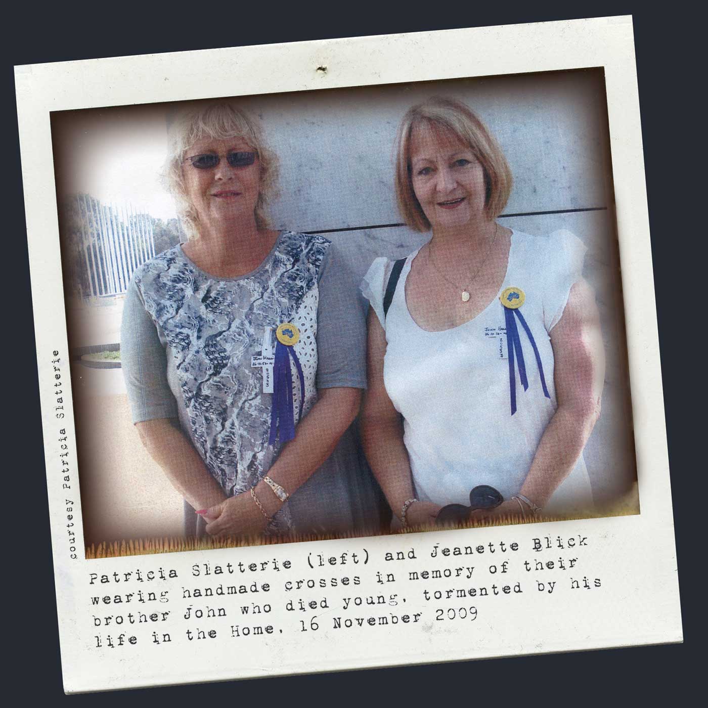 A colour Polaroid image of two women wearing badges and blue ribbons pinned to their shirts. Typewritten text below reads 'Patricia Slatterie (left) and Jeanette Blick wearing handmade crosses in memory of their brother John who died young, tormented by his life in the Home, 16 November 2009.' 'Courtesy Patricia Slatterie' is typed along the left side. - click to view larger image