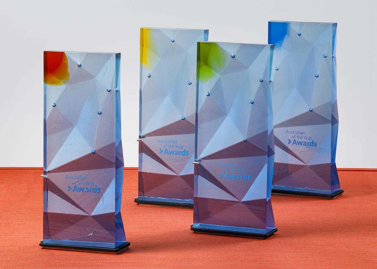 Four pale-blue glass trophies with faceted fronts. Each trophy has a different colour glass feature top left.  - click to view larger image