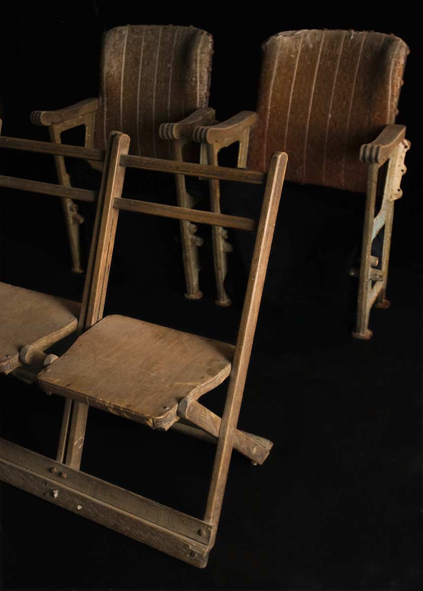 Two rows of conjoined theatre seating. Two plain wooden chairs stand at the front. Two plusher upholstered chairs at the back. - click to view larger image