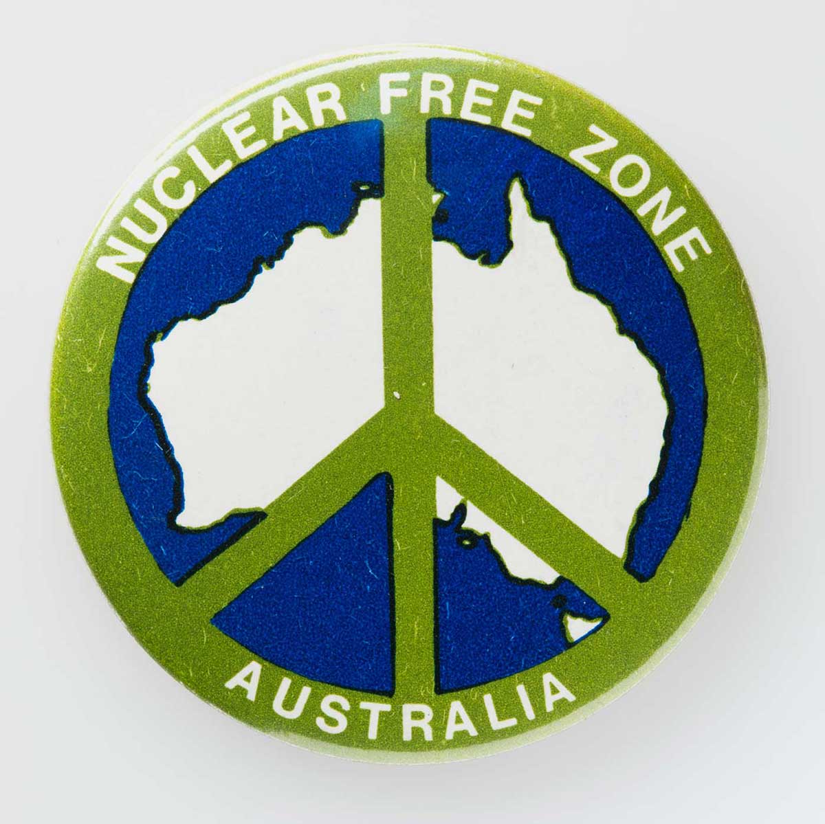 Colour photo of a badge featuring an illustration of a peace sign overlapping the Australian continent. On the edge of the badge is the text ‘NUCLEAR FREE ZONE’. - click to view larger image