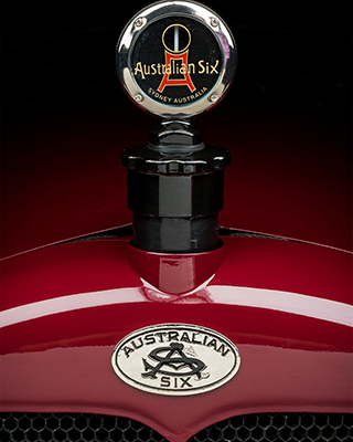 View of a polished red motor car bonnet and badge that reads ‘Australian Six’.