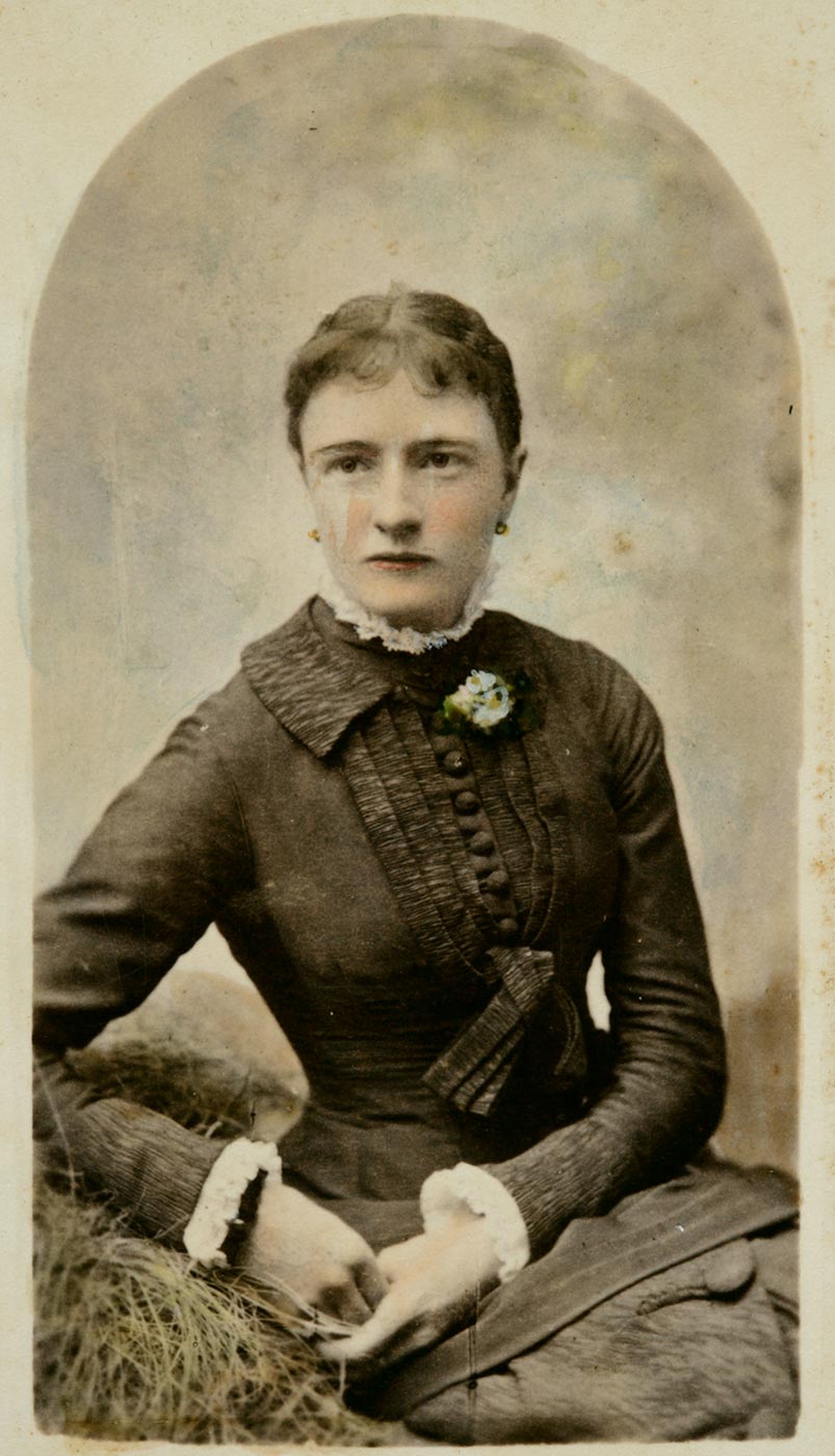 Black and white photograph of woman seated looking to the right with right arm bent and resting on a lounge and both hands clasped together. - click to view larger image