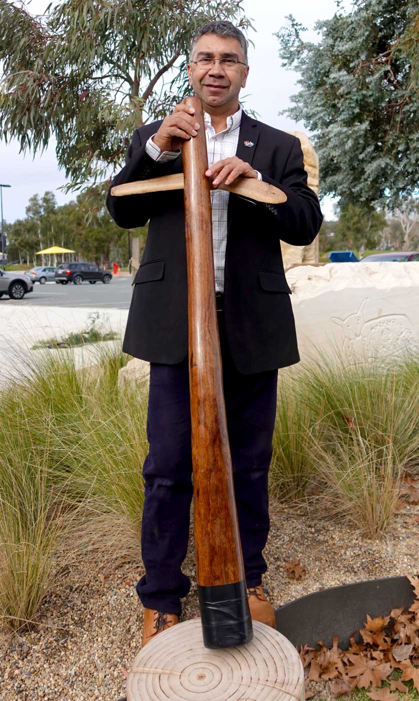 A man is standing in a garden holding a didgeridoo. - click to view larger image
