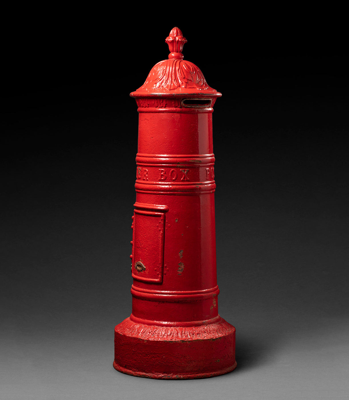 A cylindrical red post box, tapering at the top.