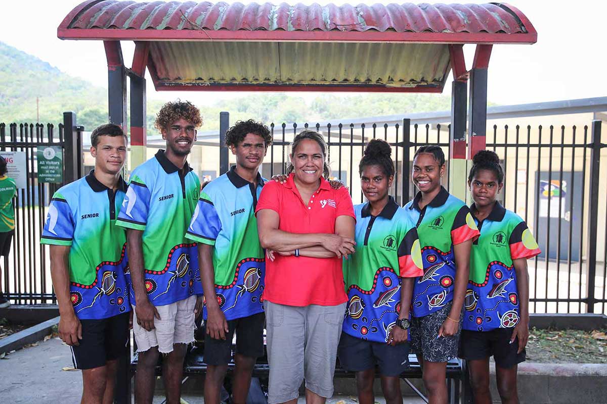 Cathy Freeman posing with a group of young people who are wearing sport uniforms.