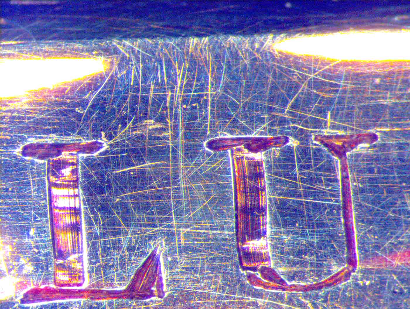 Image of magnification of a coin showing the letters 'LU' on a scratched surface. - click to view larger image