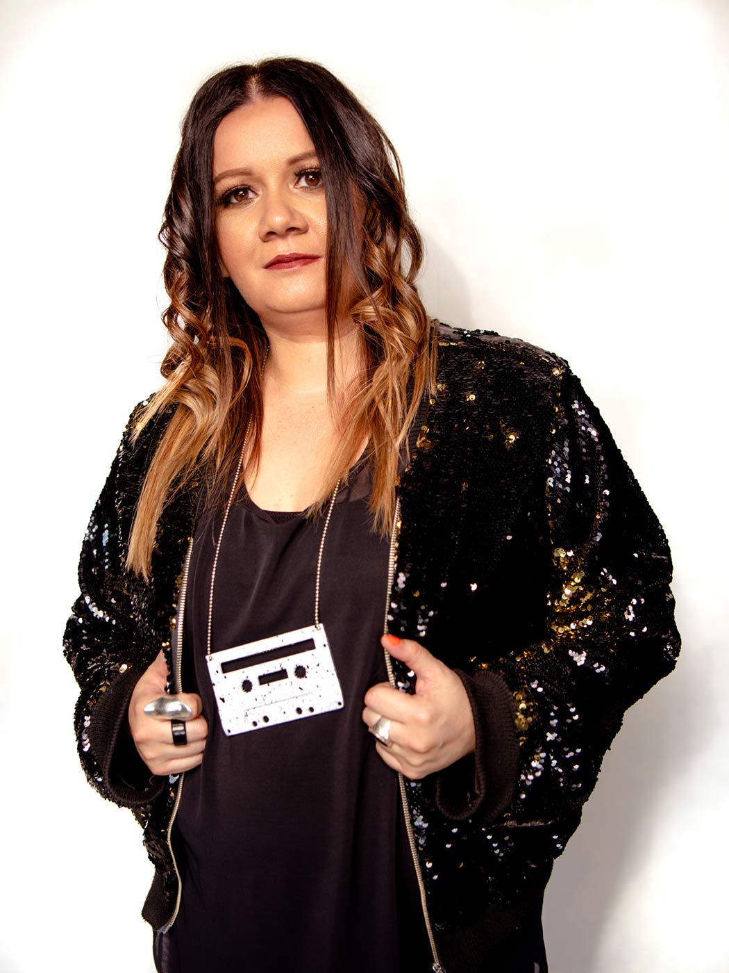 Portrait of a woman wearing a sequinned jacket and a necklace made from a cassette tape. - click to view larger image