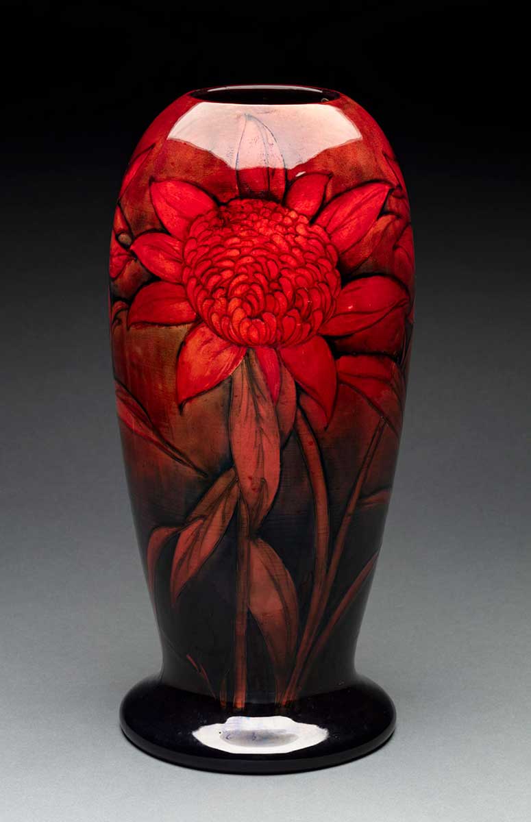 A vase featuring a rich flambe glaze and decorated with red waratahs. The exterior is painted in shades of red, black and blue, and the interior is dark red in colour. Cracking can be seen underneath the glase and there are also a few faults. - click to view larger image