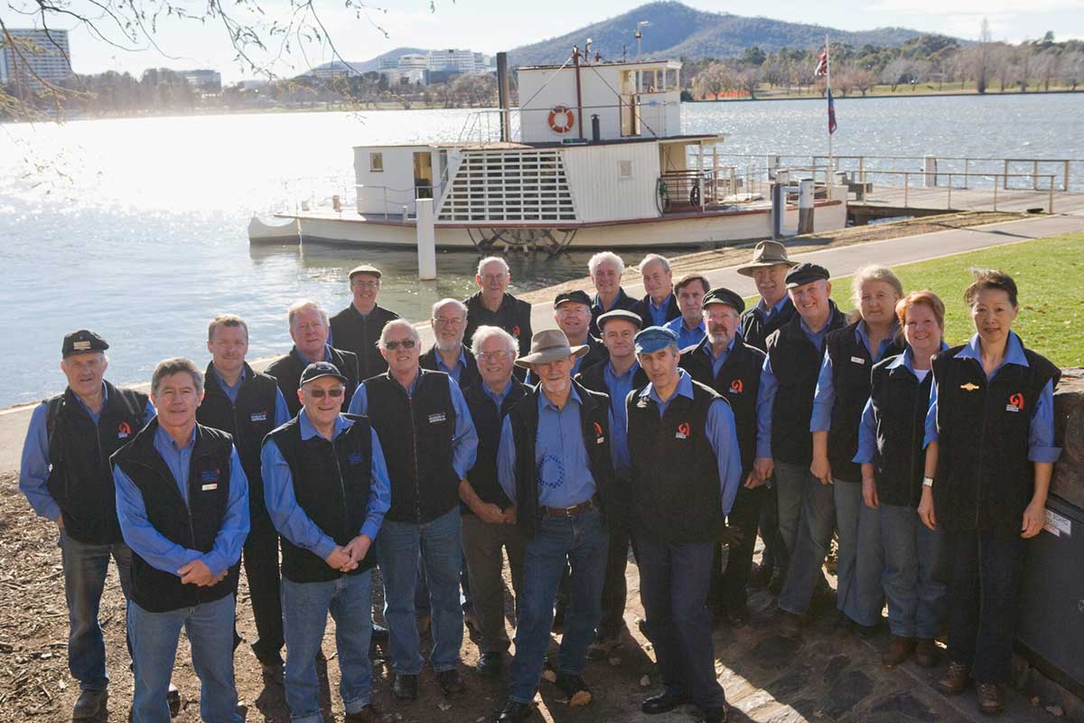 Group photo of the PS Enterprise crew with the Paddle Steamer docked in the background on Lake Burley Griffin. - click to view larger image