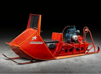 An over-snow Polaris Sno-Traveler, model K95 painted red with yellow pin stripes. The vehicle has metal sledge tracks at the front and a caterpillar track and wooden skis at the back. There is a latched door in front of the windscreen. The open driver&rsquo;s cab has a half steering wheel, brake and throttle levers and an ignition switch on the right of the dashboard. The driver's seat is upholstered in black leather and the seat back is the fuel container. The engine is mounted behind the fuel container and a winch is mounted on the rear of the wooden skis. Logo with text painted in white and black on front left and right hand side reads &lsquo;POLARIS / SNO-TRAVELER&rsquo;. Text on badge logo in centre of steering wheel reads &lsquo;POLARIS&rsquo;. Printed white text on dashboard reads &lsquo;U.S. Patent No. 2,970,662 / Canadian Patent No. 639,475 / U.S. Canadian and Other / Patents Pending&rsquo;. Text on side of engine reads &lsquo;KOHLER / U.S.A.&rsquo;.